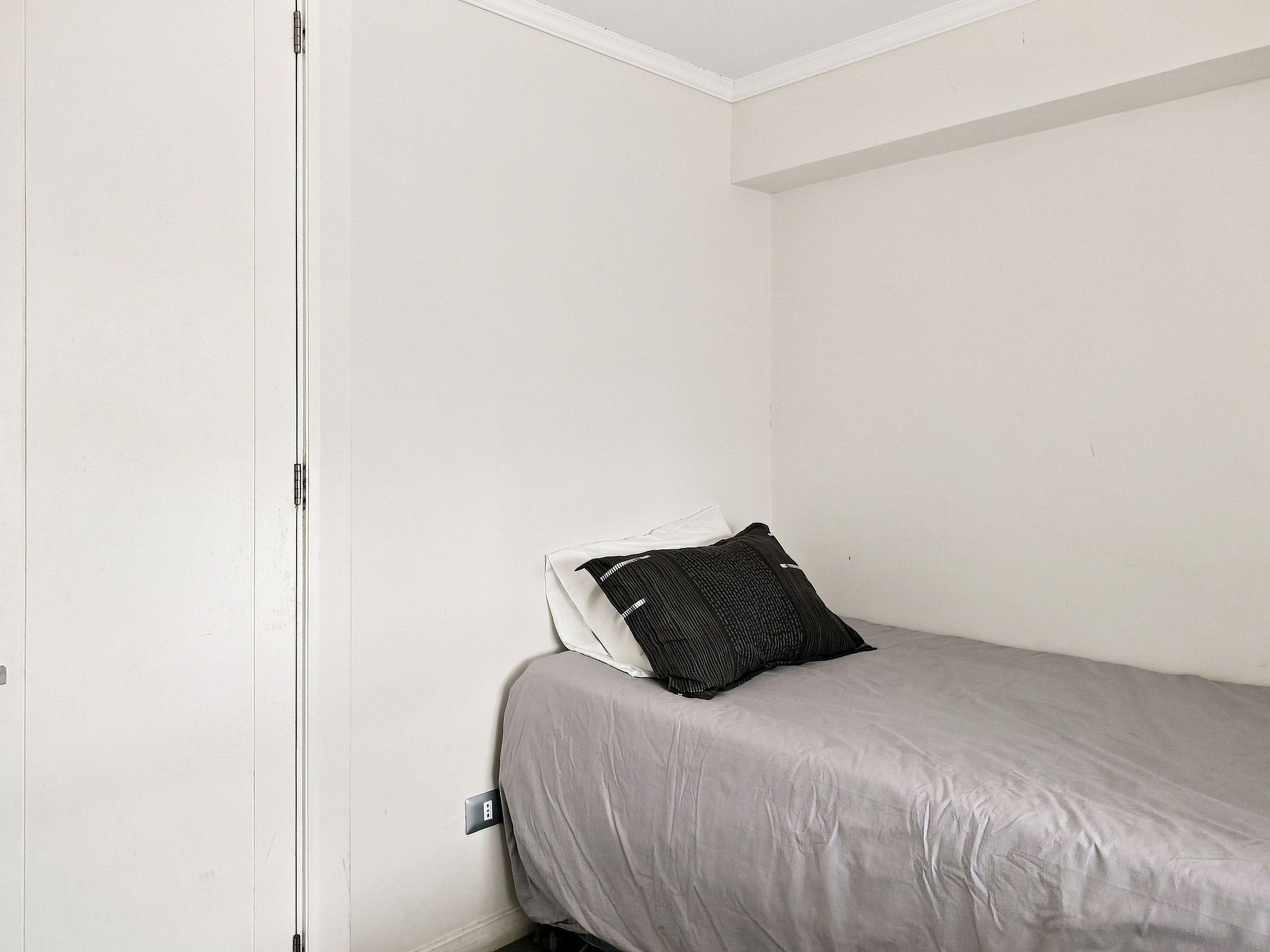 A small, single-bed room with a grey bedspread and a black pillow.