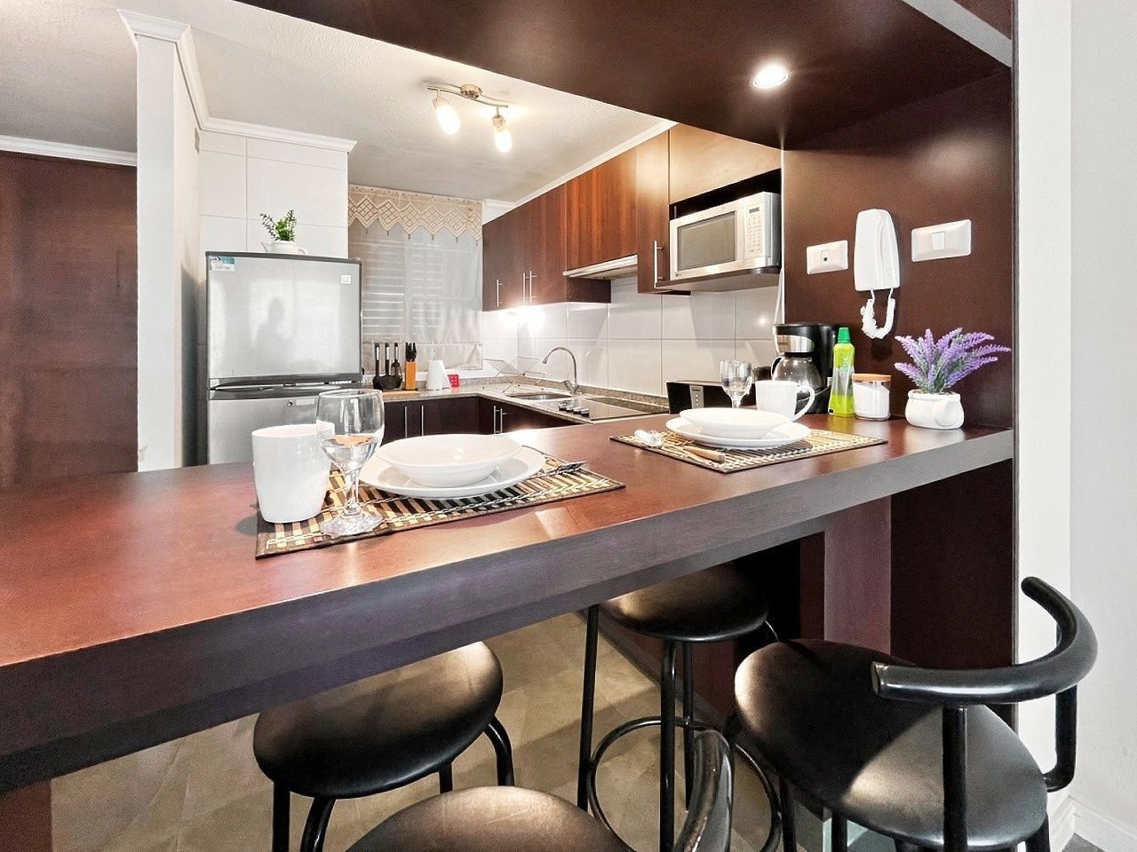 A modern kitchen with a bar area, equipped with a refrigerator, microwave, and a coffee maker.
