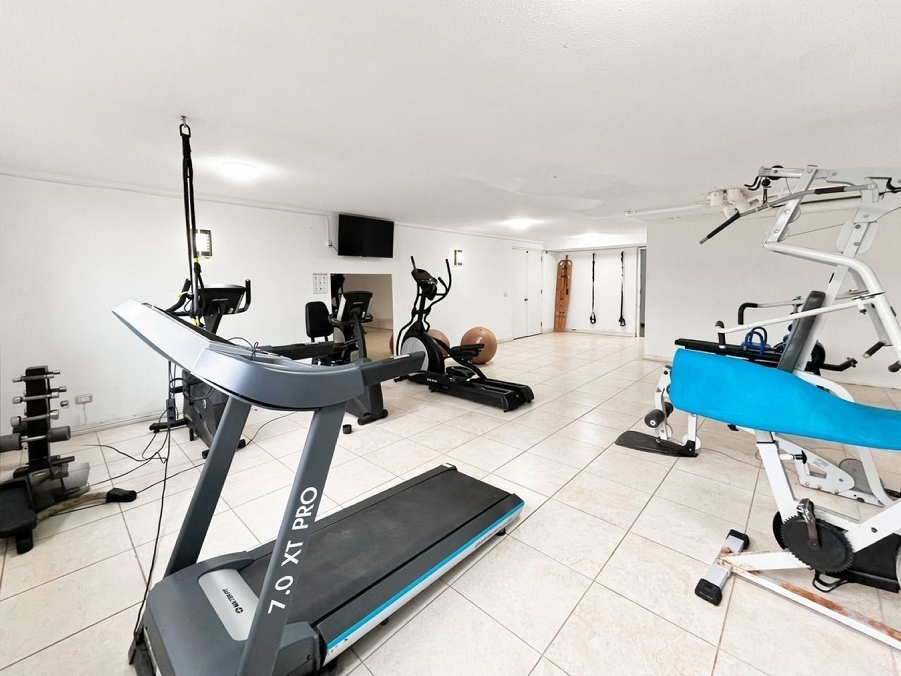 A home gym with a treadmill, stationary bike, elliptical, and weight bench.