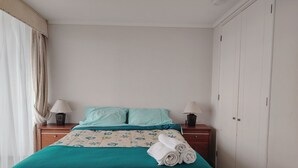 Habitación de hotel con cama, dos mesitas de noche con lámparas, armario y ventana con cortinas.