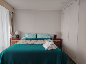 A hotel room with a bed, two bedside tables with lamps, a wardrobe, and a window with curtains. - Oceana Suites Neohaus (La Serena)
