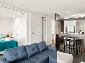 Ein modernes Hotelzimmer mit einer Sitzecke, einem Essbereich mit Hocker und einer Küchenzeile inklusive Arbeitsfläche und Geräten.
