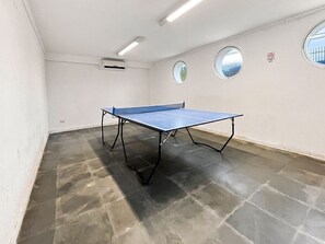 Ein Zimmer mit Tischtennisplatte, Projektor und zwei Fenstern.