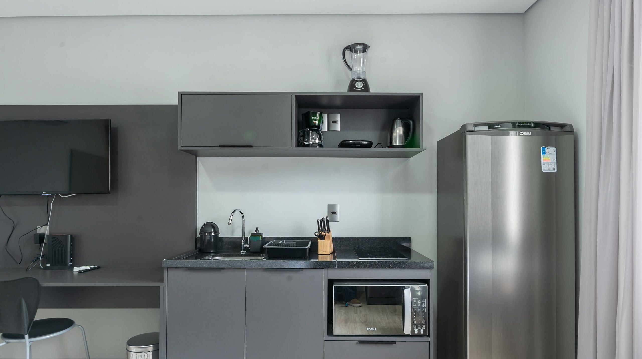 Una kitchenette compacta con microondas integrado, cafetera y refrigerador.