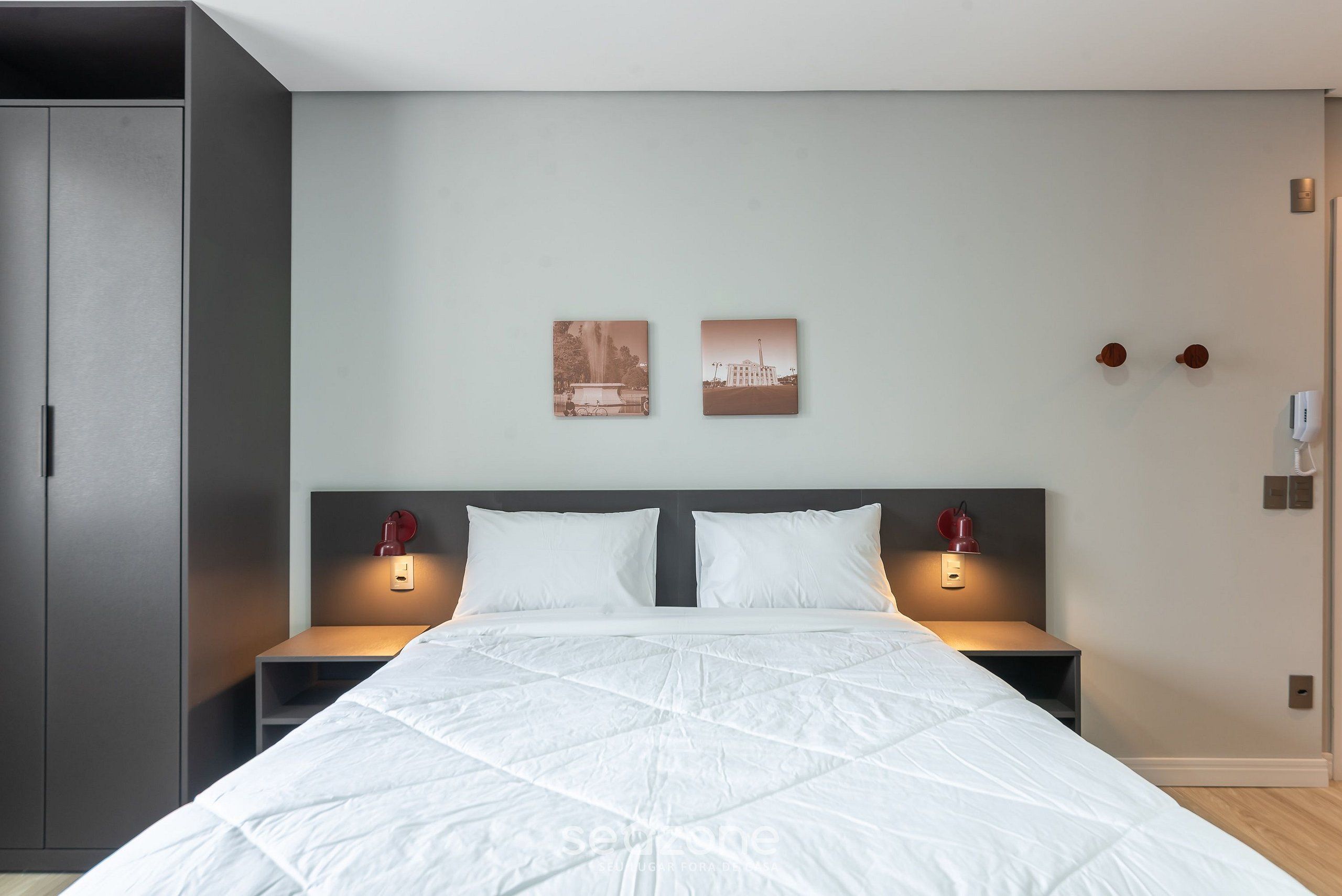 Un dormitorio moderno con una cama grande, dos mesitas de noche con lámparas rojas, un armario y dos cuadros enmarcados en la pared.