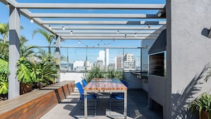 Eine Terrasse im Freien mit Tisch und Stühlen, einem Grill und Blick auf die Stadt.