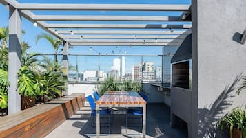 Um pátio externo com mesa, cadeiras, churrasqueira e vista para a cidade.