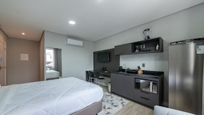 Ein modernes Hotelzimmer mit Bett, Küchenzeile und Flachbildfernseher.
