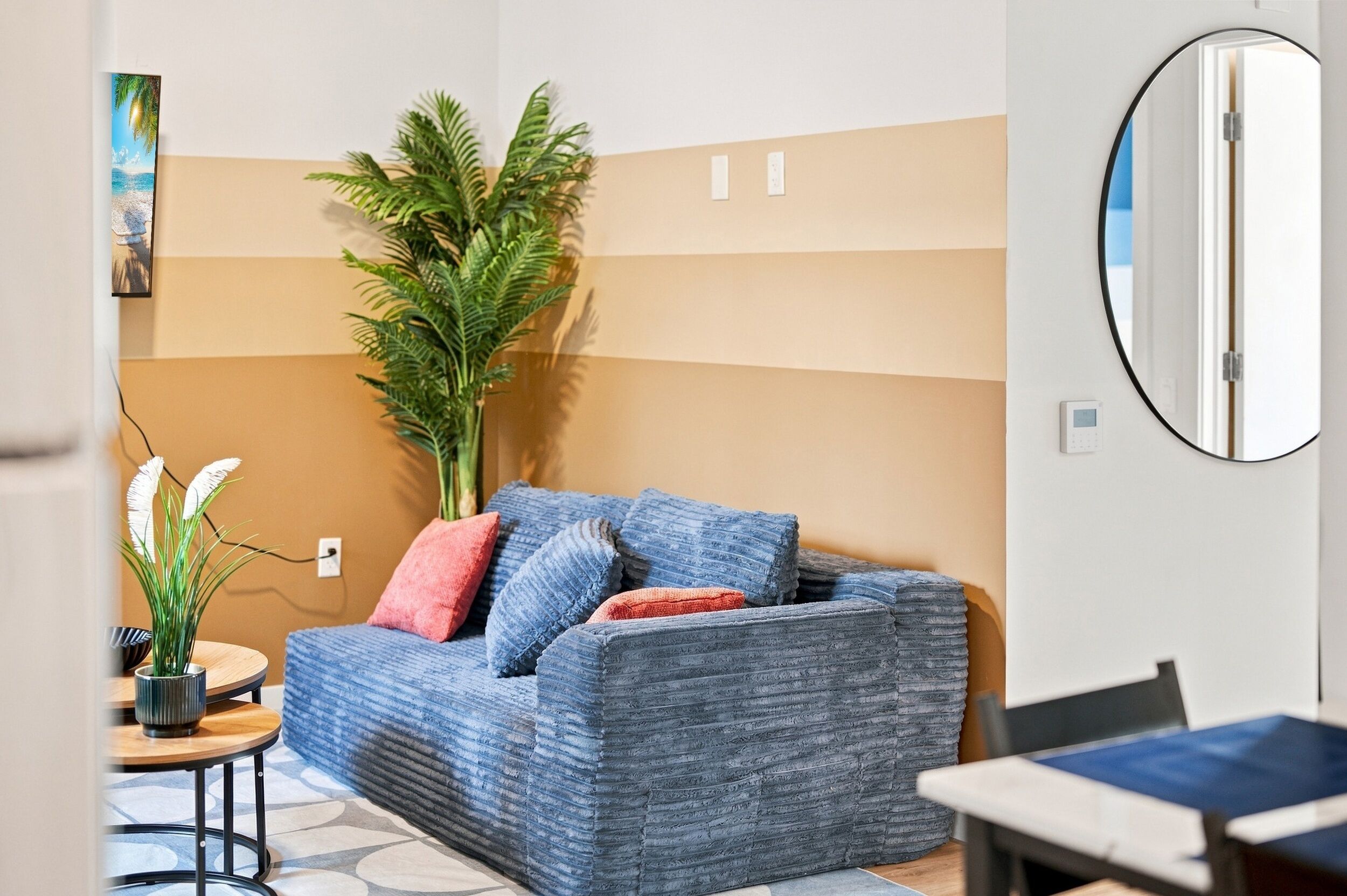 Un salon moderne avec un canapé bleu, une plante en pot et un miroir rond accroché au mur.