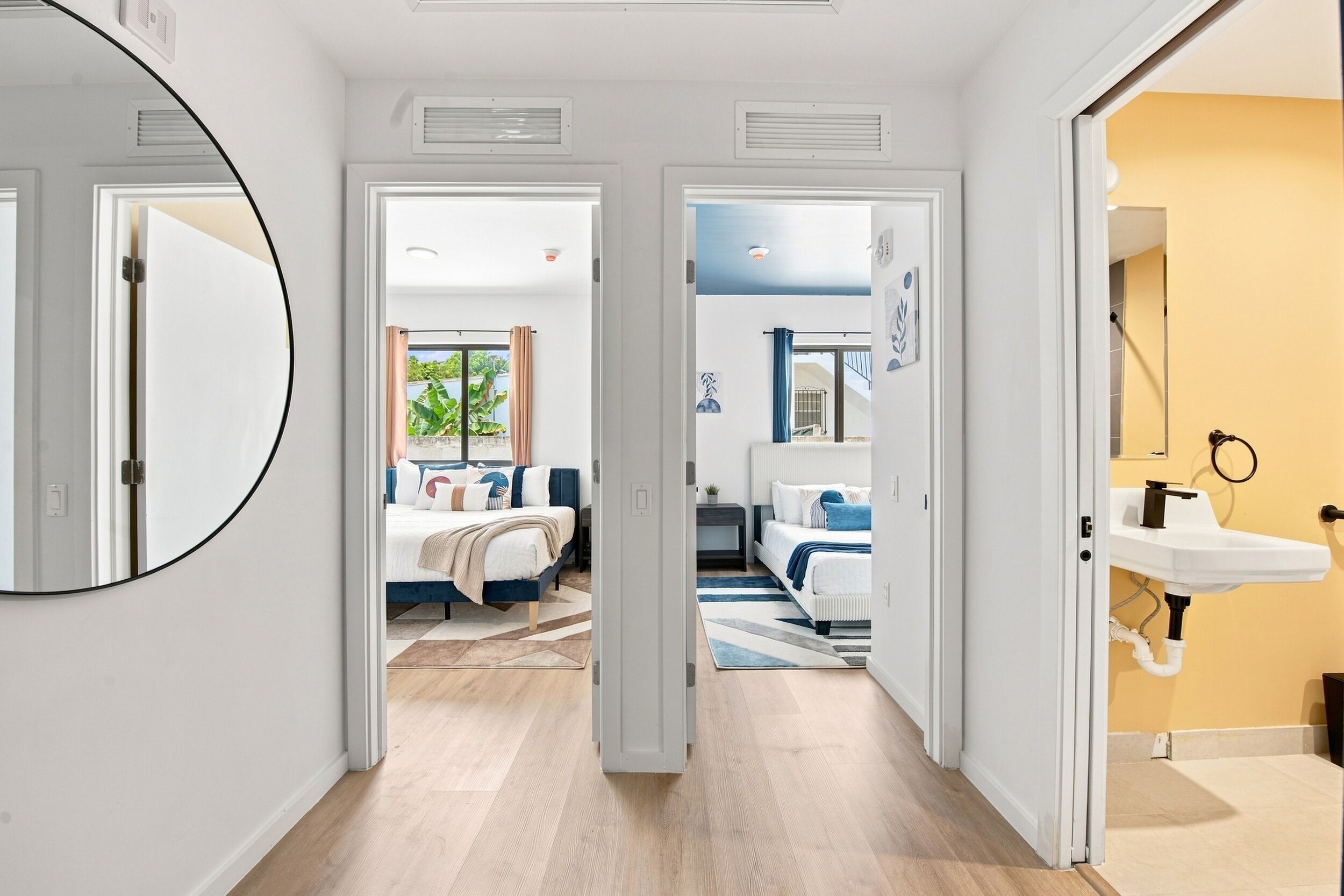A hallway leading to a bedroom with a bed, a bathroom with a sink, and a view of the outside.