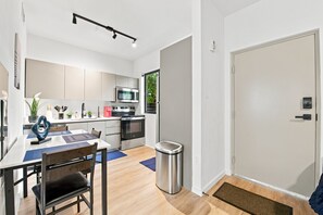 Eine moderne Küche mit Edelstahlgeräten, ein Essbereich mit Tisch und Stühlen sowie ein Mülleimer.