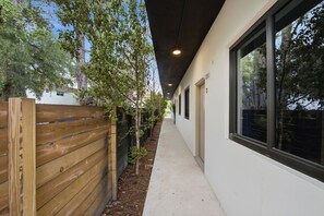 Ein Korridor mit Holzzaun, Betonweg und einem Gebäude mit großen Fenstern.
