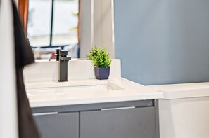 Ein Badezimmer mit einem weißen Waschbecken, einem schwarzen Wasserhahn und einer kleinen Topfpflanze.