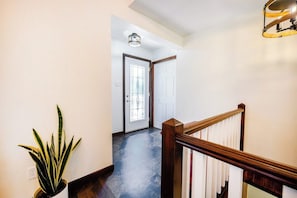 Un pasillo con una escalera, una planta en maceta y una puerta con un panel de vidrio.