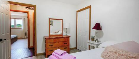 Un dormitorio con cama, cómoda, espejo, lámpara y una puerta que da a otra habitación.
