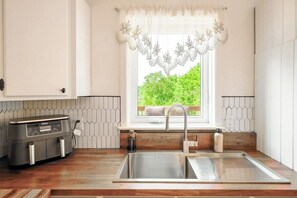 A kitchen with a built-in coffee maker, a stainless steel sink, and a window with a decorative valance.
