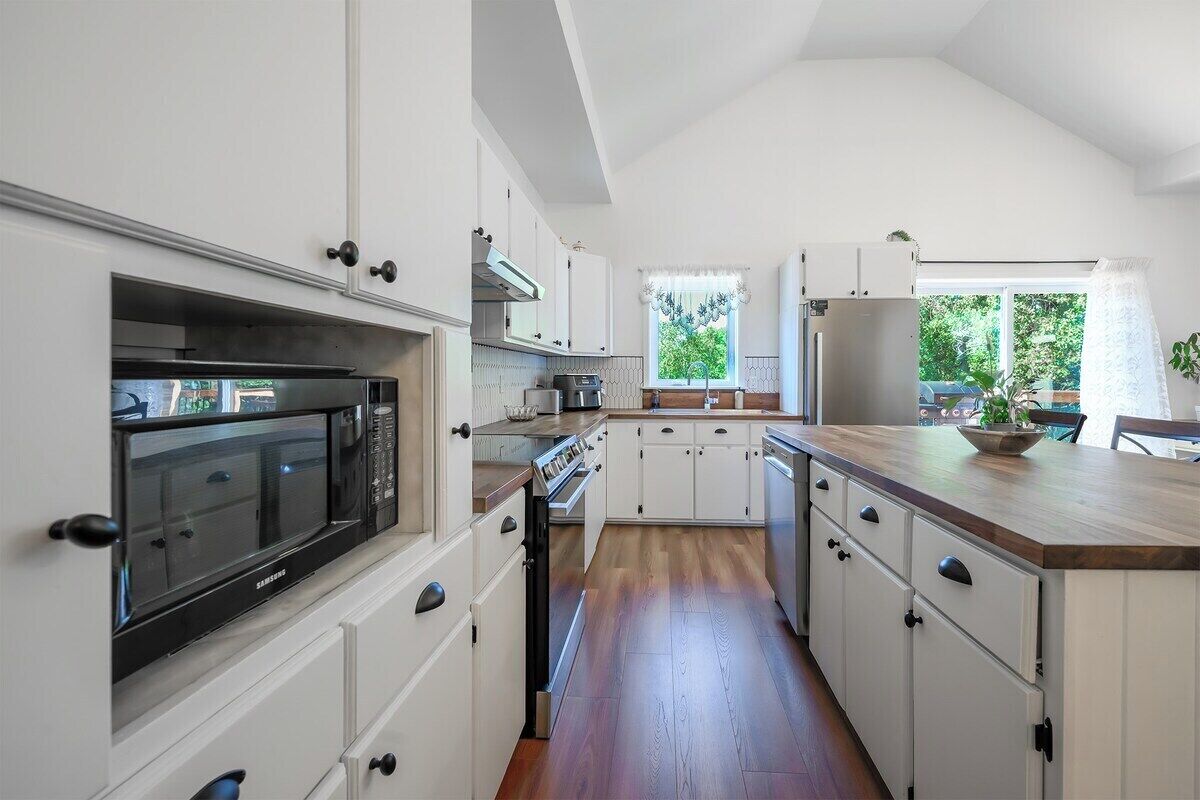 A modern kitchen with white cabinetry, a built-in microwave, and a wooden countertop.