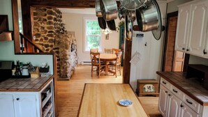 A rustic kitchen with stone walls, wooden flooring, and a dining area with chairs.