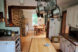 A rustic kitchen with stone walls, wooden flooring, and a dining area with chairs.