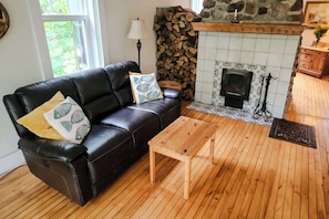 A cozy living room with a black leather sofa, wooden coffee table, and a fireplace with a stone surround. - Le Refuge du Parc | 5 min Parc Mauricie (Maskinongé Regional County Municipality)