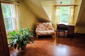A room with a wooden floor, a chair with a floral pattern, a desk, and a potted plant. - Le Refuge du Parc | 5 min Parc Mauricie (Maskinongé Regional County Municipality)