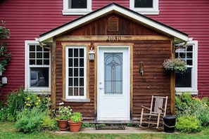 A wooden house with a white door, number 2030, and a small porch with potted plants and a rocking chair. - Le Refuge du Parc | 5 min Parc Mauricie (Maskinongé Regional County Municipality)