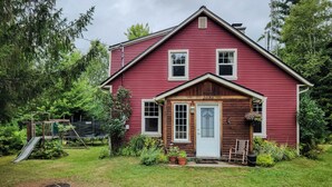 A red wooden house with a number 2030 on the front door, surrounded by a grassy yard and trees.