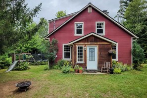 A red wooden house with a number 2030 on the front door, surrounded by a grassy yard and trees.