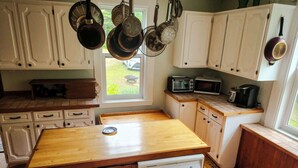 A kitchen with white cabinets, a wooden countertop, a dishwasher, a microwave, and hanging pots.