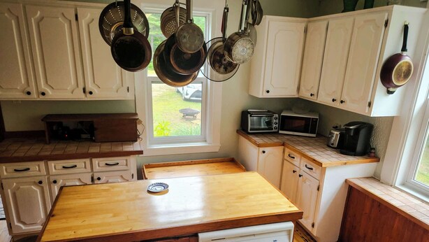 A kitchen with white cabinets, a wooden countertop, a dishwasher, a microwave, and hanging pots.