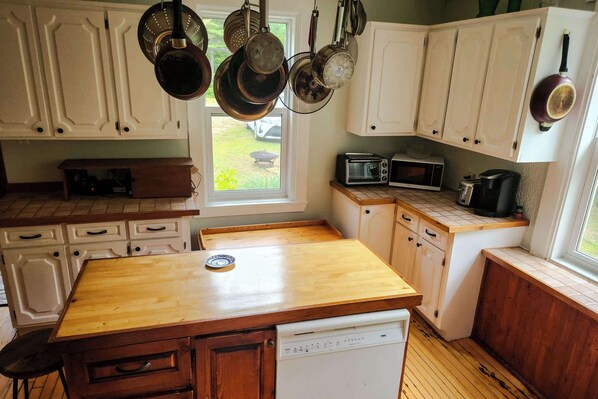 A kitchen with white cabinets, a wooden countertop, a dishwasher, a microwave, and hanging pots.