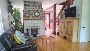 A living room with a fireplace, wooden flooring, a sofa, a television, and a staircase.