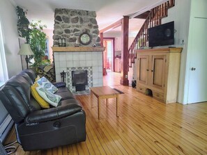 A living room with a fireplace, wooden flooring, a sofa, a television, and a staircase.