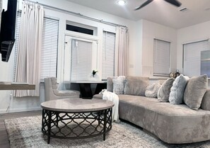 A modern living room with a curved sofa, a round coffee table, and a ceiling fan. - Quaint Duplex near everything medical center , downtown , pearland (Houston)