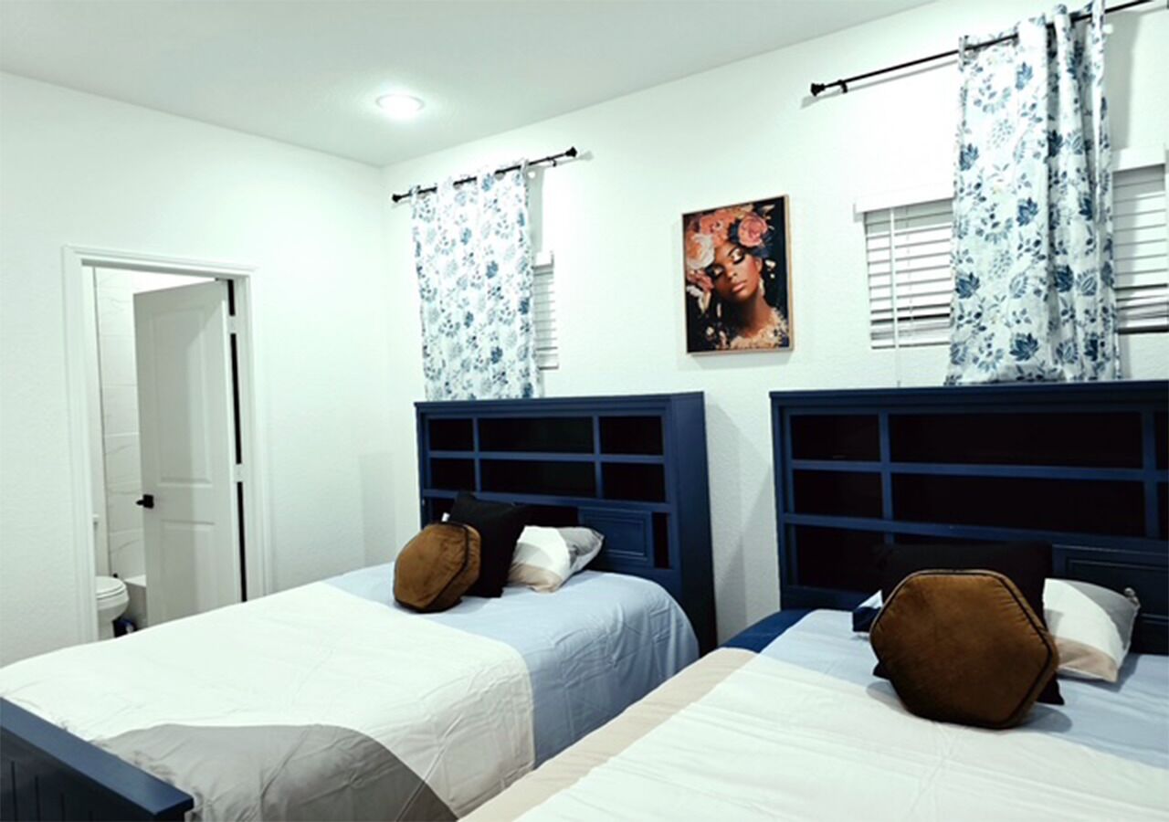 A bedroom with two beds, a door to a bathroom, and a window with curtains.
