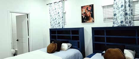 Een slaapkamer met twee bedden, een deur naar een badkamer en een raam met gordijnen.