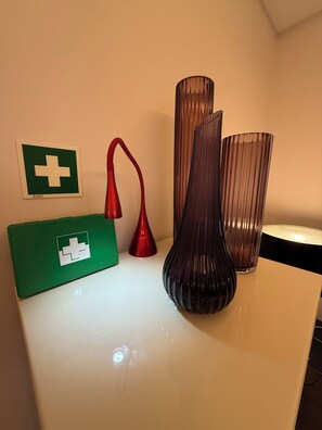 Ein weißer Tisch mit drei Vasen, einer roten Lampe und einem grünen Kasten mit einem weißen Kreuz-Symbol.