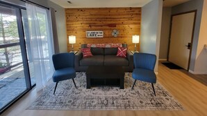 Ein modernes Wohnzimmer mit einer Holzvertäfelung, zwei blauen Stühlen, einem schwarzen Sofa und einem gemusterten Teppich.