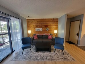 Ein modernes Wohnzimmer mit einer Holzvertäfelung, zwei blauen Stühlen, einem schwarzen Sofa und einem gemusterten Teppich.