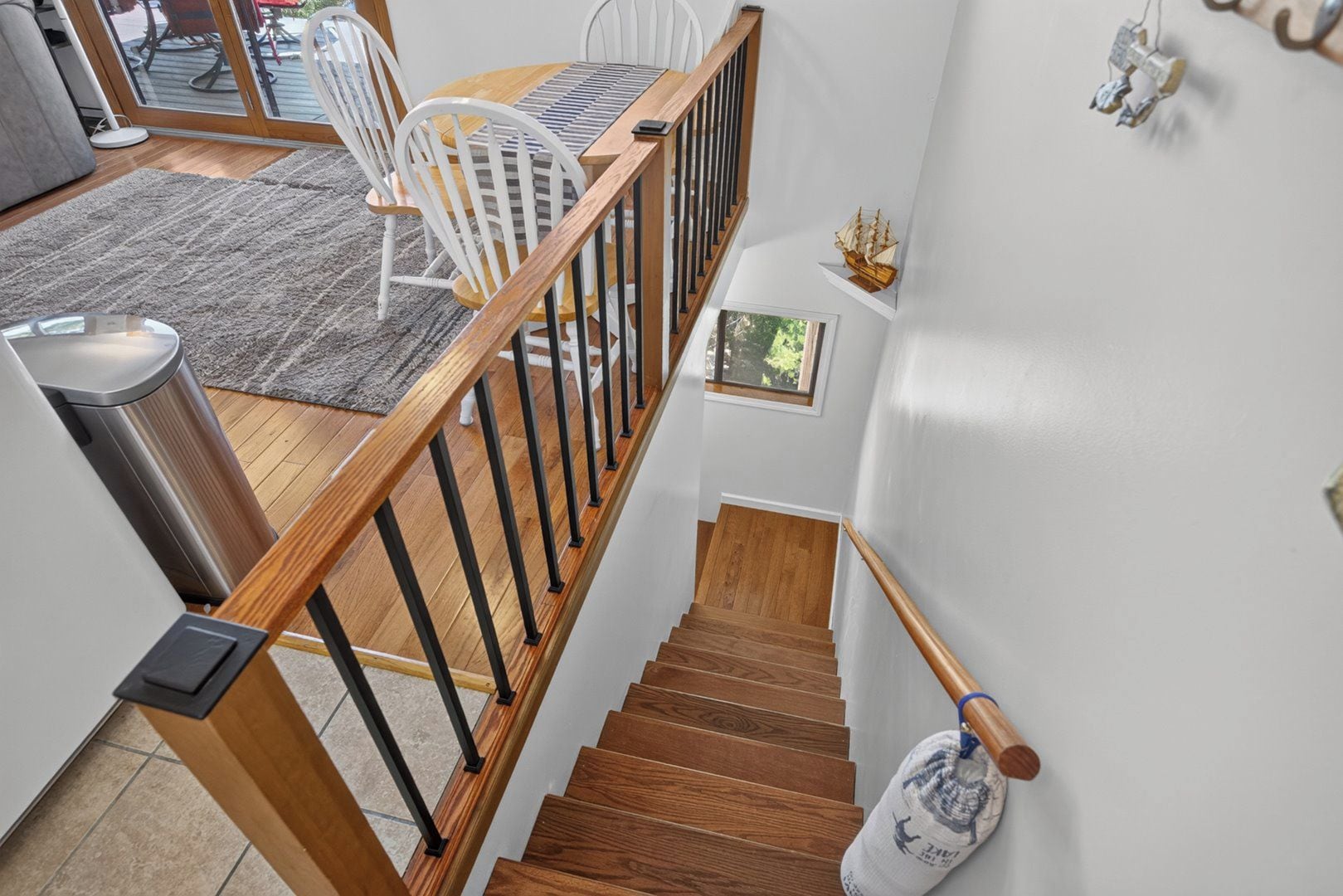 A staircase with wooden steps and black railings, leading to a dining area with white chairs and a wooden table.