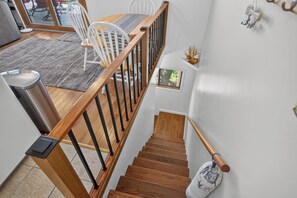 Eine Treppe mit Holzdielen und schwarzen Geländern, die zu einem Essbereich mit weißen Stühlen und einem Holztisch führt.