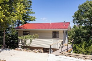 Ein eingeschossiges Haus mit rotem Dach, einer Veranda und einem kleinen Garten mit Vogeltränke.