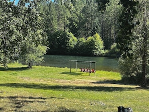 A grassy area with a swing set and a pond surrounded by trees.