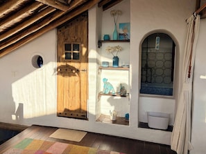 A rustic room with a wooden door, a small shelf with decorative items, a window with a blue-tiled design, and a wooden ceiling. - Iechie Historic Colonial Stay in La Candelaria (Bogotá)