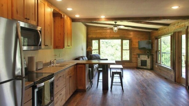 A spacious kitchen with wooden cabinets, a stainless steel refrigerator, and a large island with stools. - Lookout Cabin 1 (Caledonia)