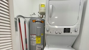 A laundry room with a stacked washer and dryer, a water heater, and a red mop. - Spacious 1-Bedroom Duplex Vance Villa in UPTOWN Lexington (Lexington)