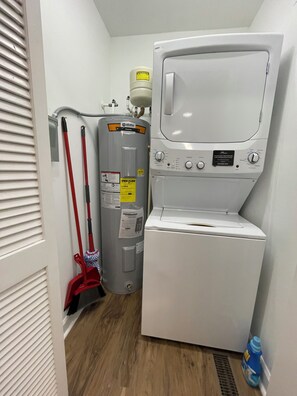 Ein Waschraum mit einer übereinander gestapelten Waschmaschine und einem Trockner, einem Warmwasserbereiter und einem roten Wischmopp.