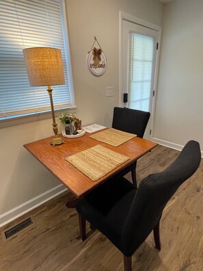 Un coin repas avec une table en bois, deux chaises noires, une lampe et un élément de décoration murale.