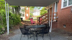 A covered patio area with a gravel floor, a round table with chairs, and a red Adirondack chair. - Spacious 1-Bedroom Duplex Vance Villa in UPTOWN Lexington (Lexington)