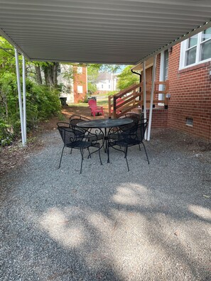 Ein überdachter Patio-Bereich mit Kiesboden, einem runden Tisch mit Stühlen und einem roten Adirondack-Sessel.